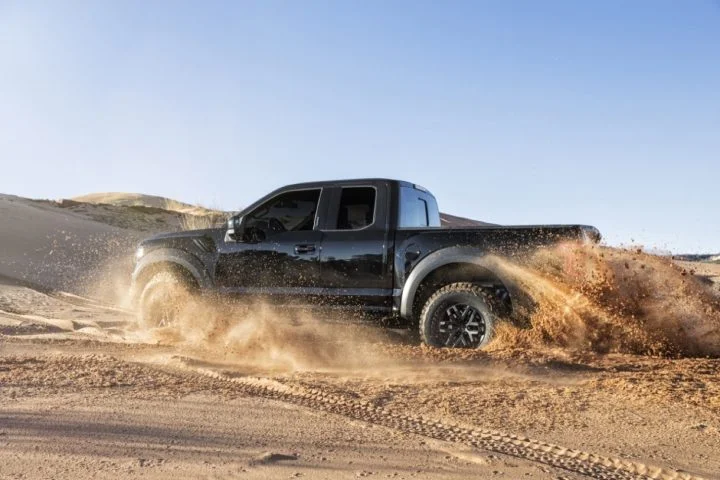 Photo of the 2017 Ford F-150 Raptor driving through sand, viewed from the driver's side. Fox shocks help keep it comfortable over rough terrain.