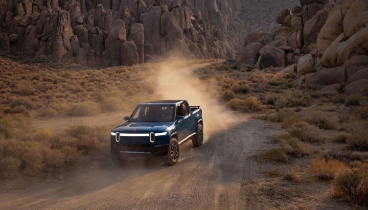 A front three quarters view of a Rivian R1T driving down a dirt road
