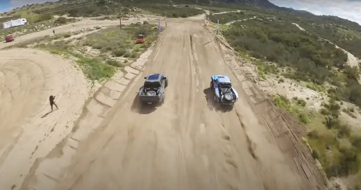 A rear view of a Ford F-150 Raptor racing a Ranger Edge off-road.