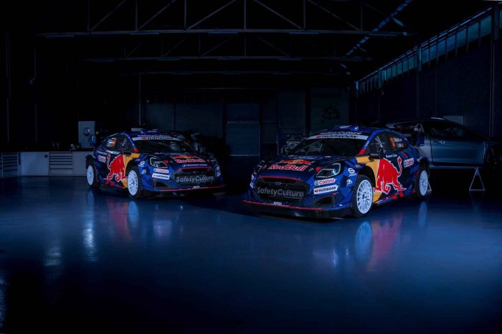 Photo of the M-Sport Ford Puma Rally1 hybrid race cars, parked at a front three-quarters angle in a dark garage. The 2025 Rally Kenya was a rough event for the team. 