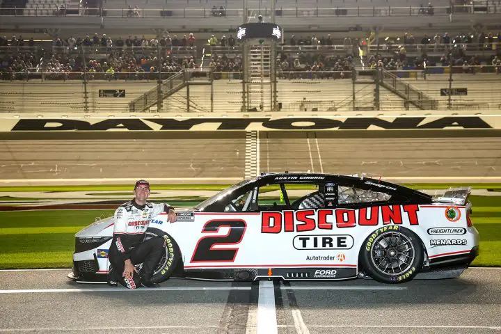 Photo of NASCAR Ford driver Austin Cindric at Daytona, posing beside his No. 2 Ford Mustang Dark Horse race car. Cindric was penalized for intentionally crashing a competitor. 