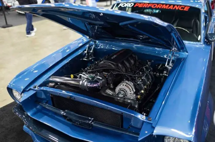 Photo of the 1965 Ford Mustang with the 7.3L V8 engine under the hood, showing its hood up and the engine in full view. 