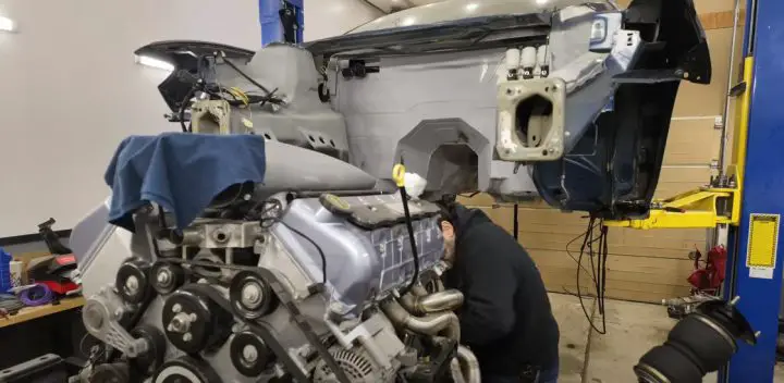 Video still of the V-10 swapped Lincoln Continental, shown with the body perched on a lift and the engine in the foreground. The custom build is the brainchild of Build It Yourself on YouTube.