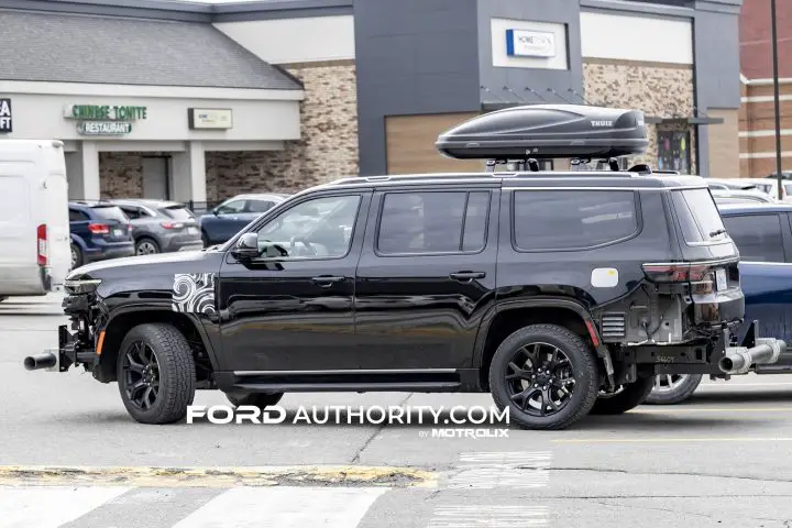 Photo showing the Jeep Wagoneer EREV prototype undergoing testing, featuring light camo and missing front and rear fascias, seen from a side angle. 