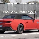 2026 Ford Mustang GT with camo covering the 5.0 and pony badges, pictured from the rear passenger side.