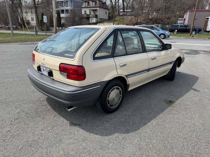 A photo showing the exterior of a 1989 Mercury Tracer hatchback from a rear three quarters angle.