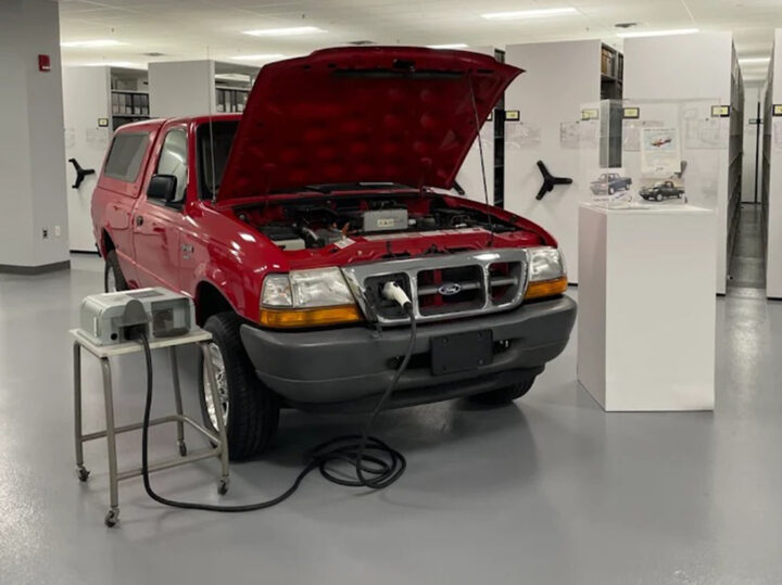 Photo of the 2000 Ford Ranger EV parked in the U.S. Heritage Fleet collection, shown with its hood up and plugged into a charger. 