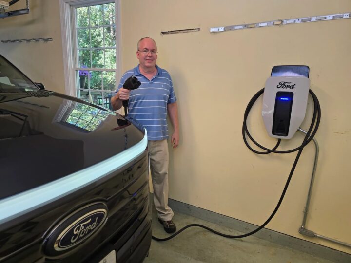 A photo showing the exterior of a Ford F-150 Lightning and charger from a front angle.